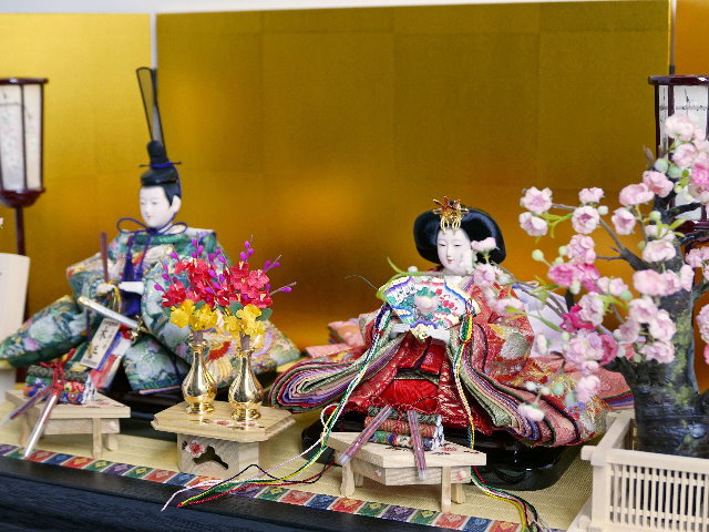 華やかな鳳凰の刺繍が特徴の雛人形を金屏風と黒塗り台に並べる収納飾り