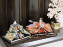 鳳凰を刺繍した生地を贅沢に使用した豪華な雛人形です。茶塗りの六曲屏風屏風と桜の木で宴のように飾りました。