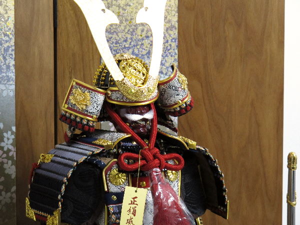 黒い小札を黒糸で威した渋めのコンパクト大鎧を箔散らし桜絵で飾る五月人形