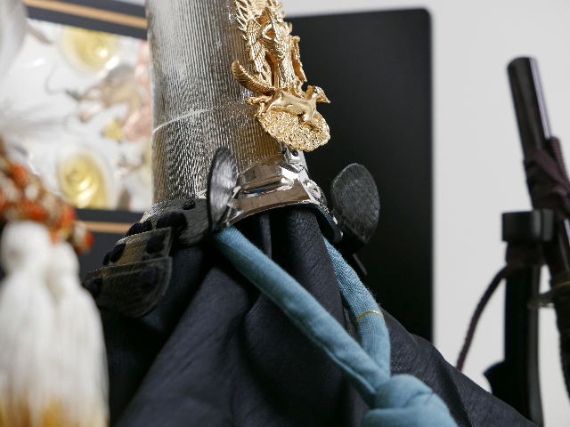 上杉謙信公仕様の銀烏帽子形兜を三曲の彫金龍虎屏風と一本矢弓太刀で黒塗りの収納台に並べた五月人形です。