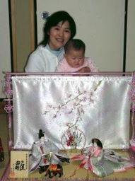 女の子の赤ちゃんをひざに抱き、おしゃれな雛人形の後ろに座って記念写真